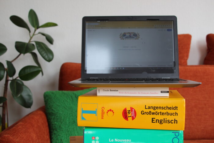 Ein Laptop steht auf einem Stapel aus Wörterbüchern auf einem kleinen Tisch vor einer Couch.